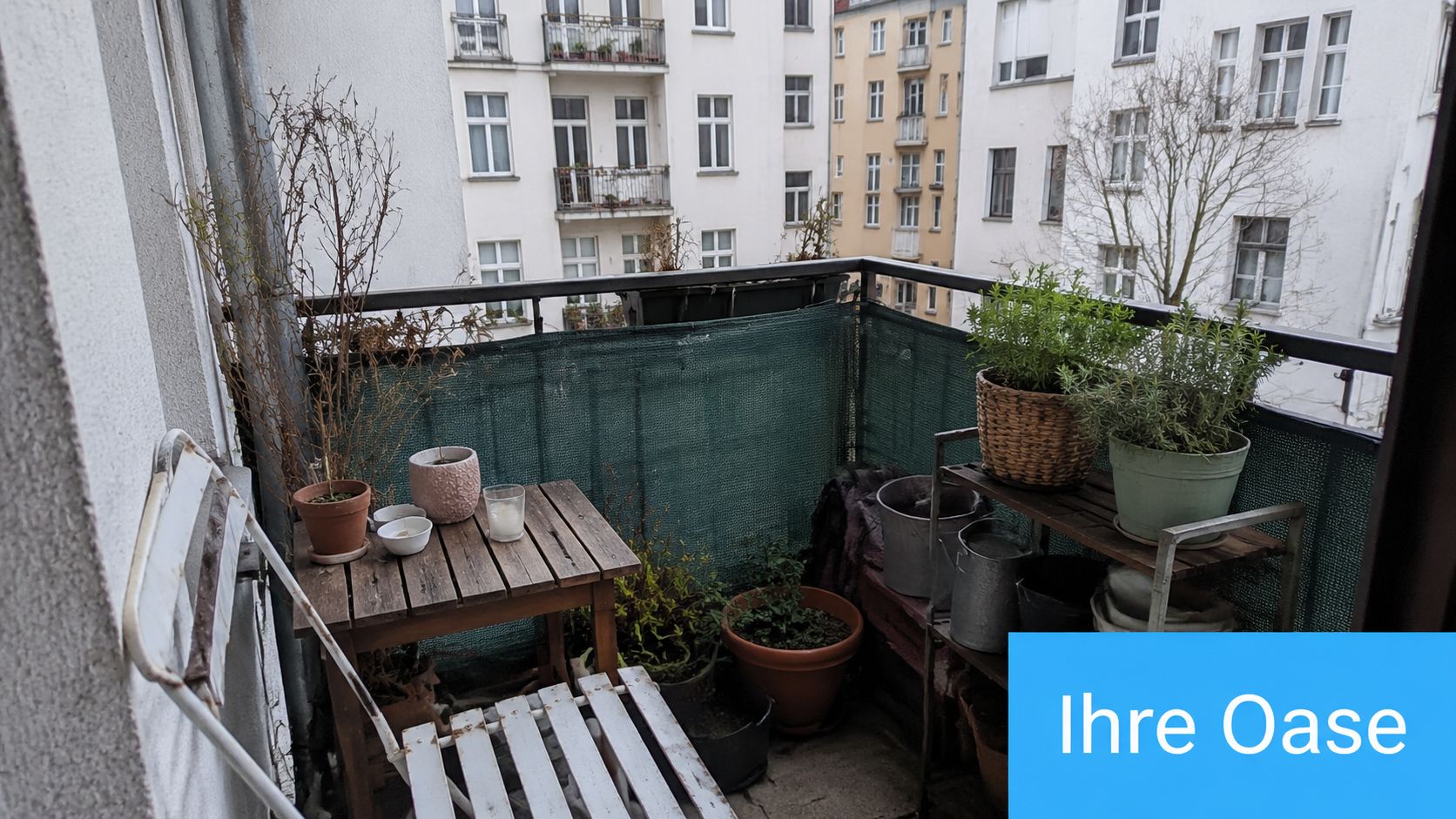 Balkon Sichtschutz mit Motiv: Ratgeber & Ideen 2026 3 Ein gemütlich eingerichteter Balkon mit Pflanzen, kleinen Möbeln und einem grünen Sichtschutz vor einem Wohngebäude.